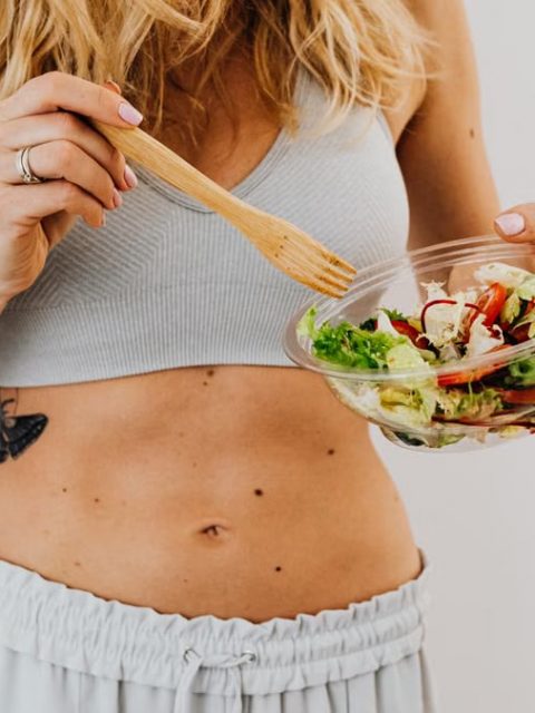Young woman in sports attire holding a fresh salad bowl, promoting a healthy lifestyle.