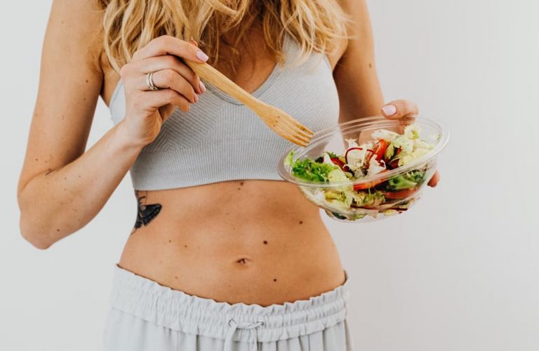 Young woman in sports attire holding a fresh salad bowl, promoting a healthy lifestyle.