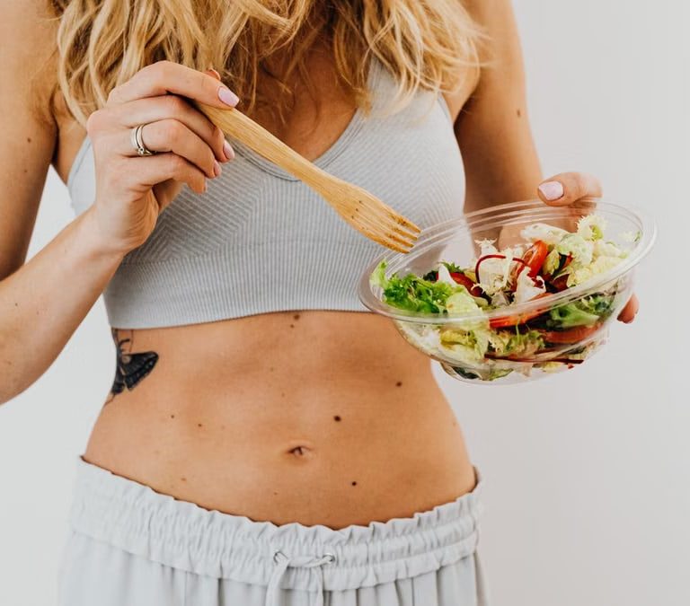Young woman in sports attire holding a fresh salad bowl, promoting a healthy lifestyle.